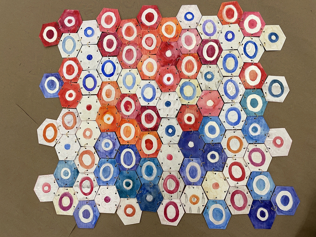 Multiple paper red, blue, and white hexagons with inscribed circles linked together. Back side.